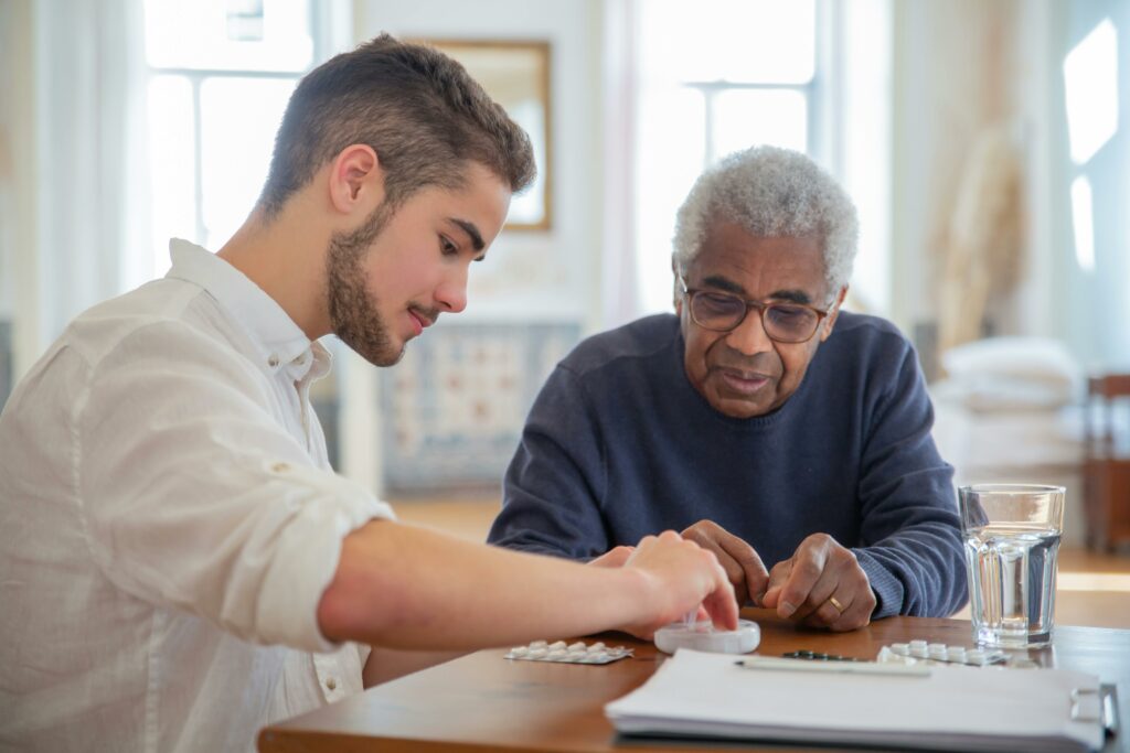 Young caregiver assisting an elderly man with medication at a care home.